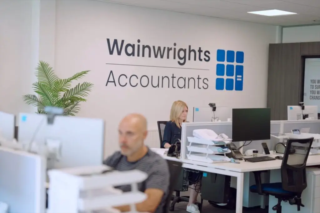 A Wainwrights accountant at her desk beneath the Wainwrights Accountants logo on the office wall