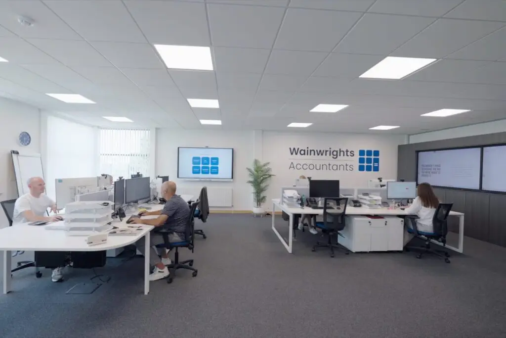 The Wainwrights Accountants team at their desks in the Bromborough office, with the firm's logo on the wall