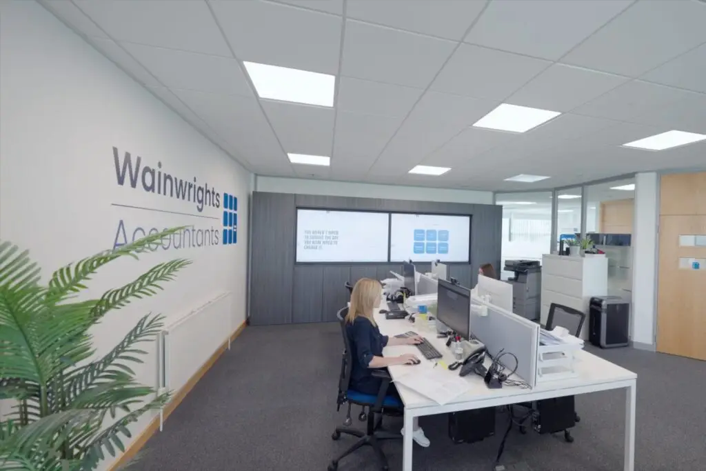 A Wainwrights accountant working at her computer, with wall screens behind her in the Bromborough office